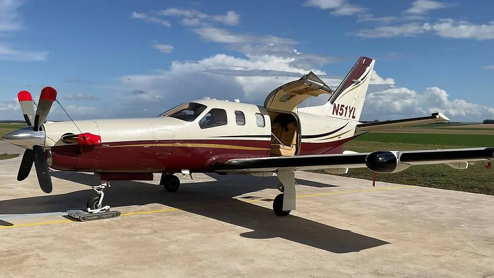 Side view of a white and maroon single-engine turboprop aircraft with its passenger door open, parked on a tarmac.