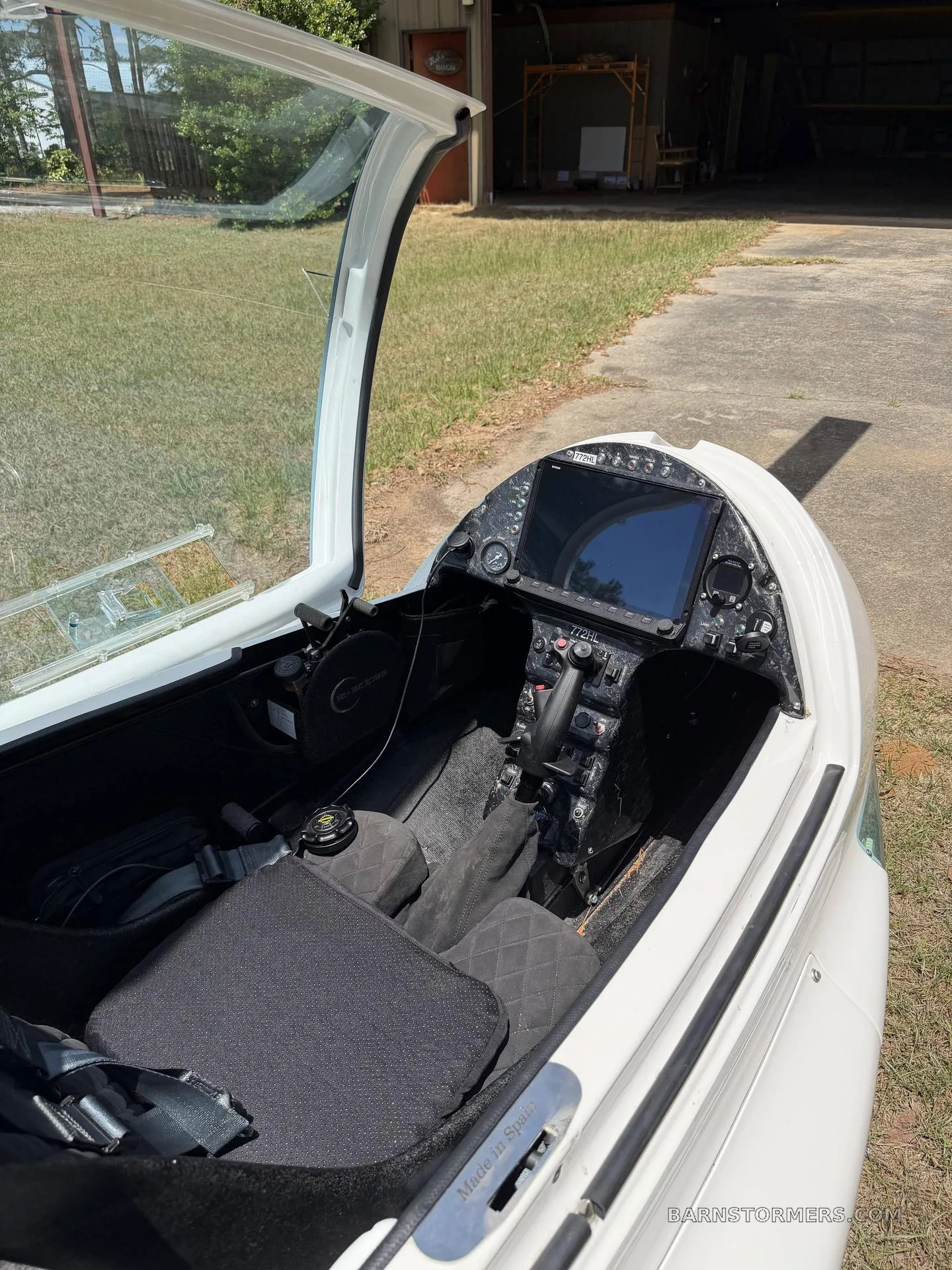 The cockpit of a white autogyro with a large digital display, control stick, and black seats, seen with the canopy open.