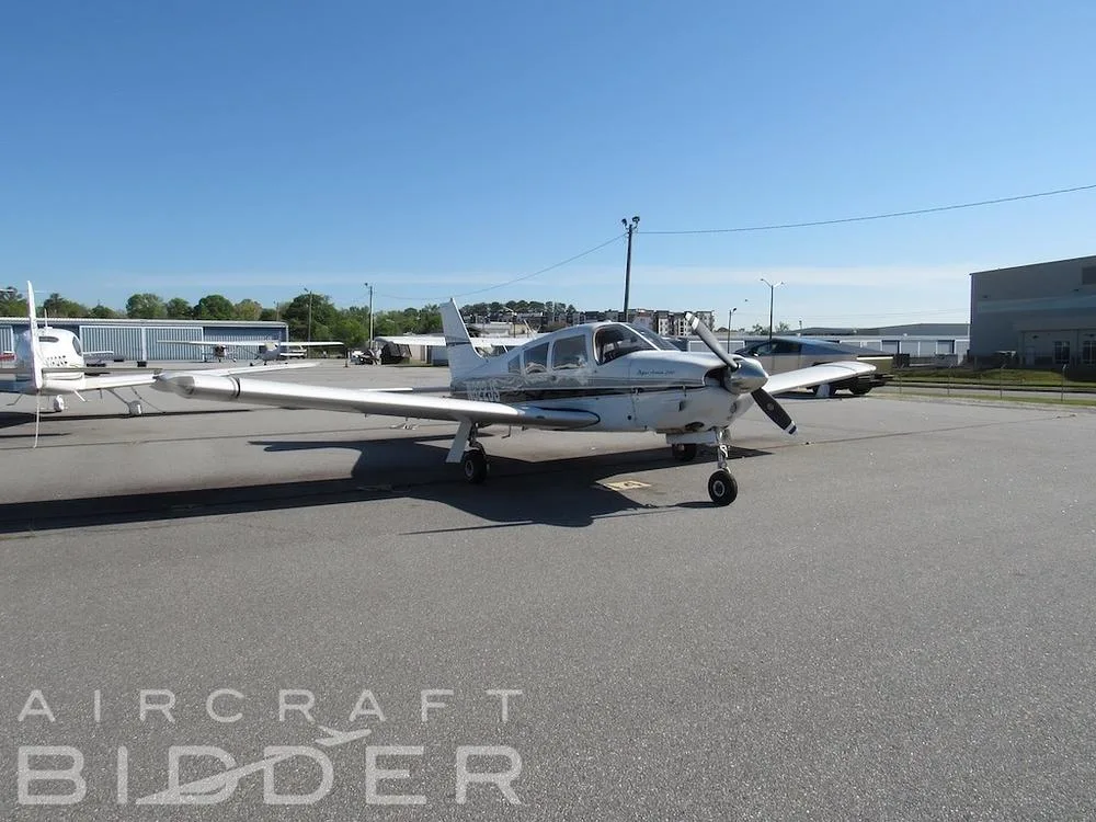 A white Piper Arrow 200 (N822JS) with black and grey stripes, parked on an asphalt tarmac on a sunny day.