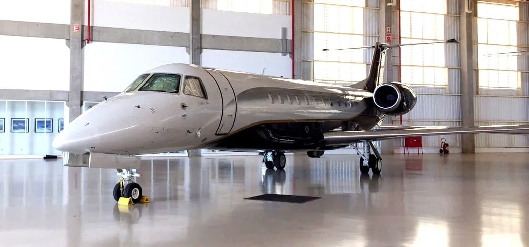 A sleek white and black business jet with tail-mounted engines, parked inside a well-lit hangar.