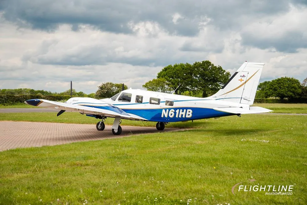 A side view of the N61HB Piper Seneca aircraft, white with blue and gold accents, parked on a tarmac.
