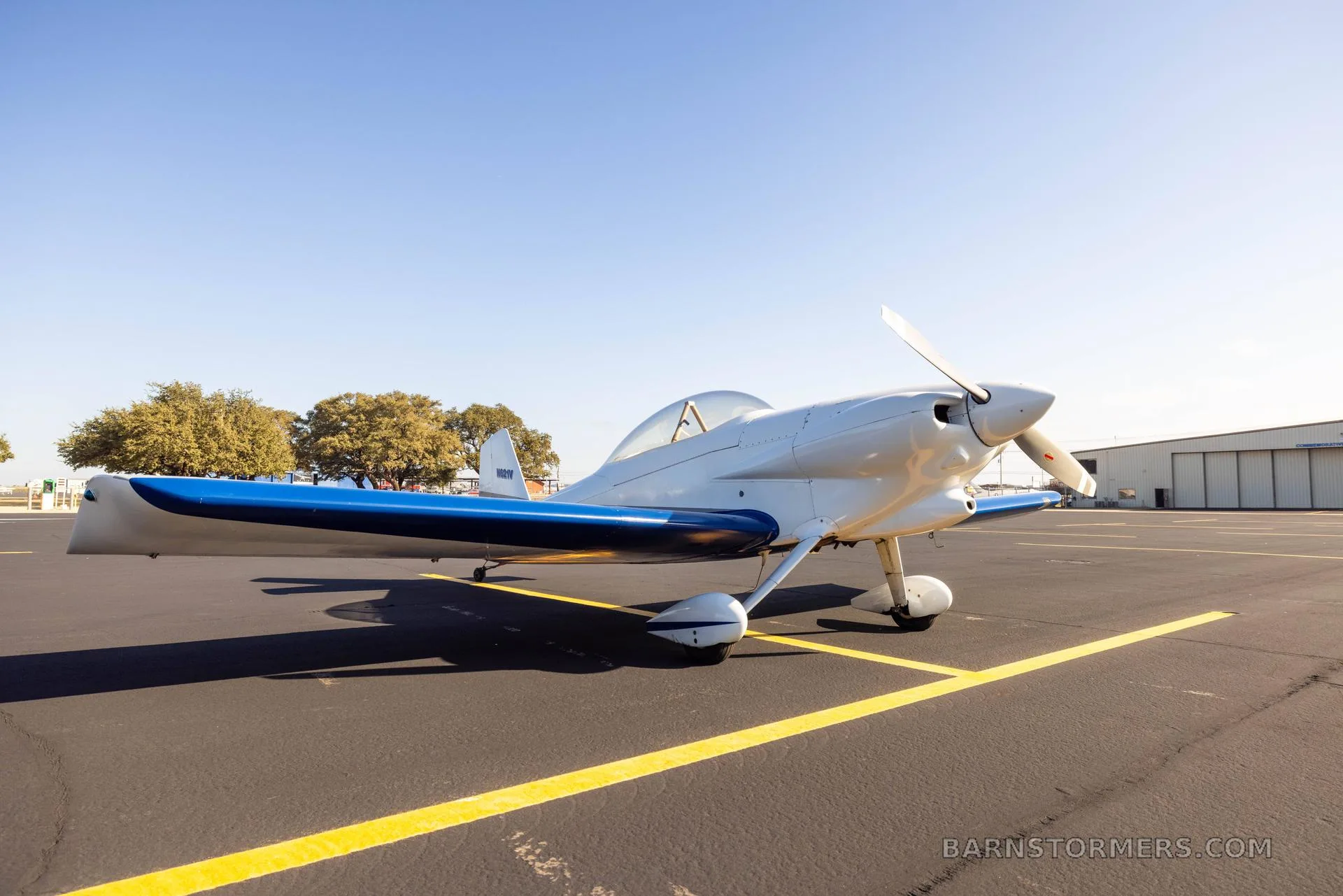A white and blue single-engine aircraft with tail number N821V parked on an asphalt tarmac.