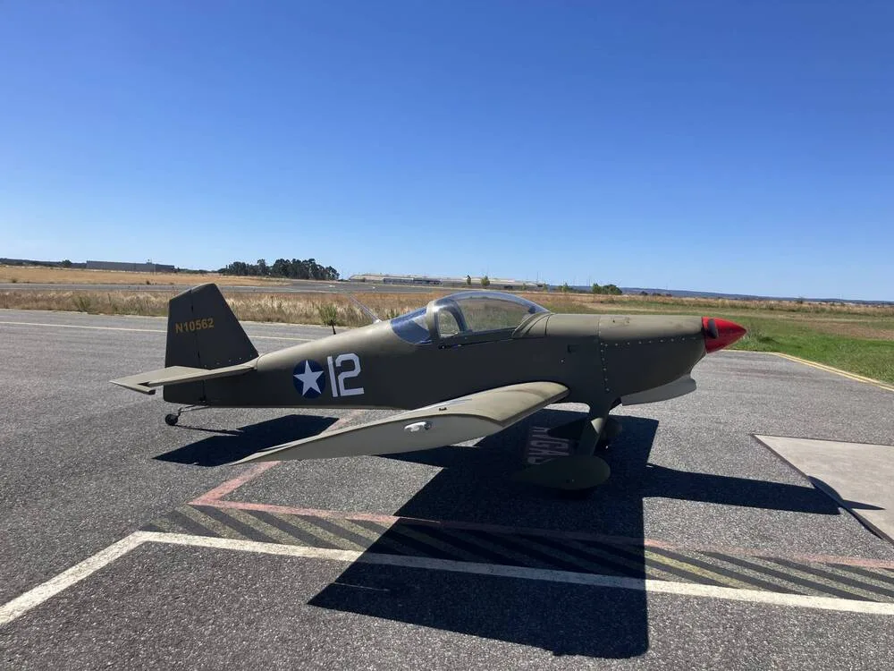 A green single-engine aircraft with a red nose and "N10562" on the tail, parked on an airfield under a clear blue sky.