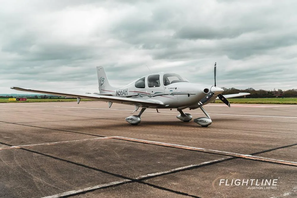 A white Cirrus SR22 aircraft with registration N56AH parked on a tarmac under a cloudy sky.