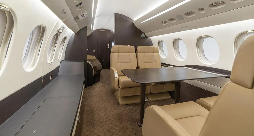 A view of the business jet's interior cabin showing tan leather seats, a dark table, and a long side console.