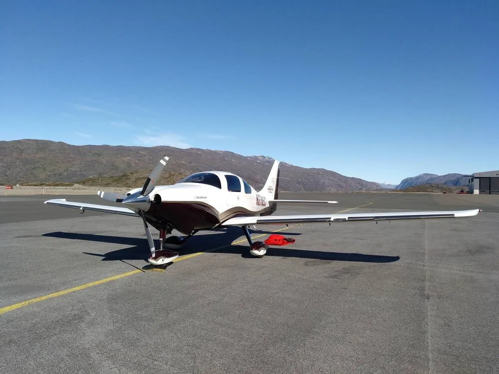 A white and brown Cirrus SR22 aircraft, N-441, parked on an asphalt runway with mountains in the background under a clear blue sky.