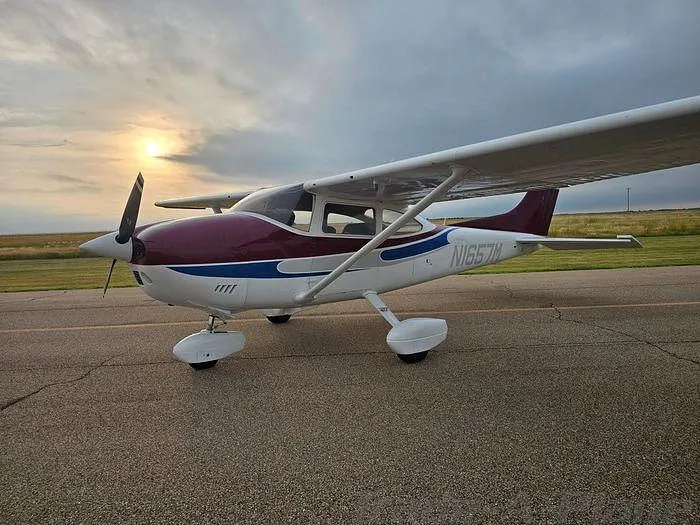 A white and maroon Cessna 182 Skylane with blue accents, parked on an airfield at sunset.
