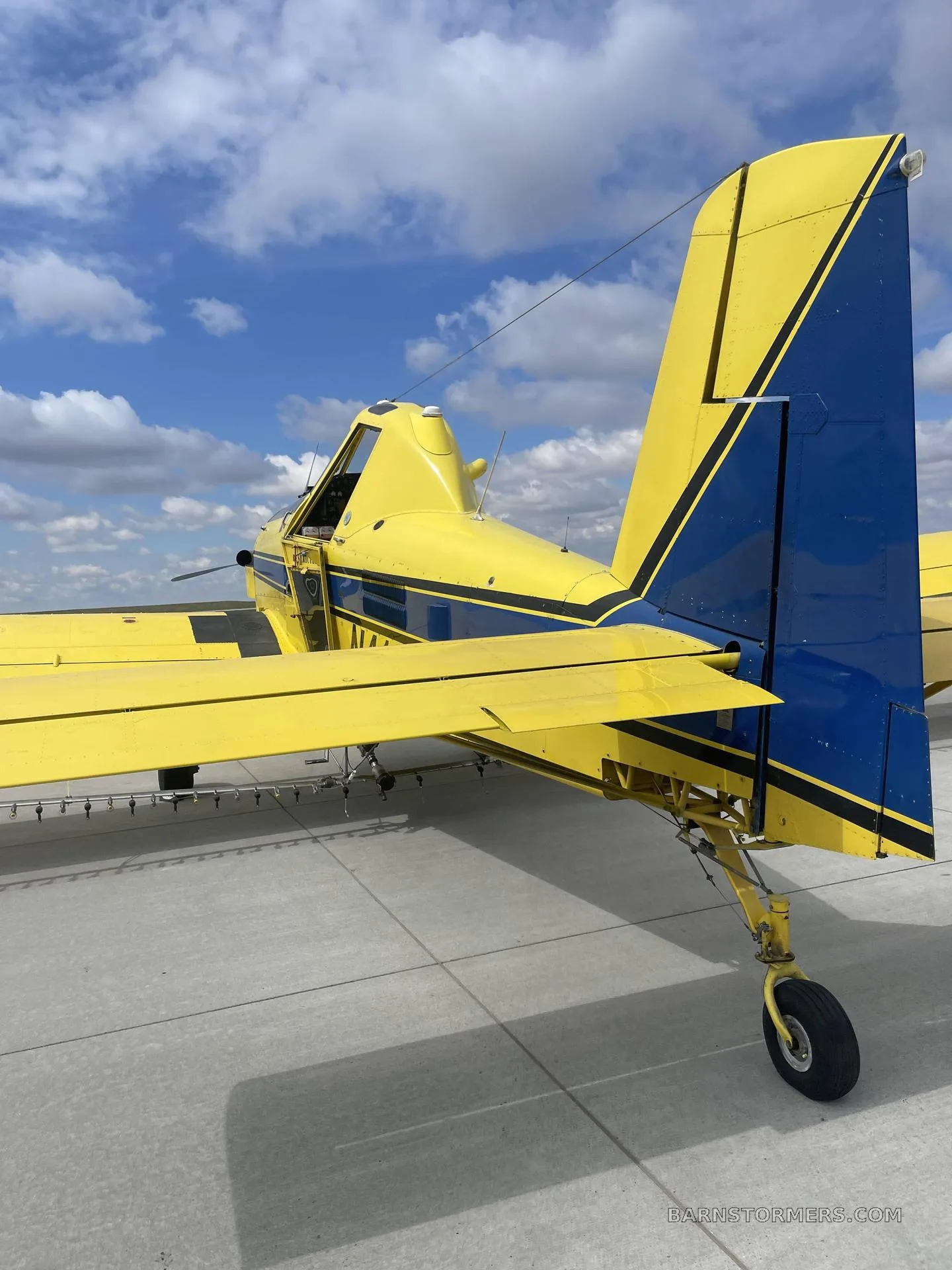 The tail section of a yellow and blue Air Tractor agricultural aircraft, showing the vertical stabilizer and tailwheel, parked on a tarmac.
