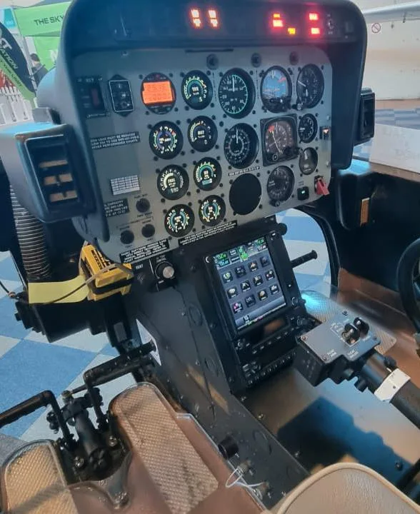 The instrument panel of a helicopter cockpit, featuring analog gauges and a modern digital display.