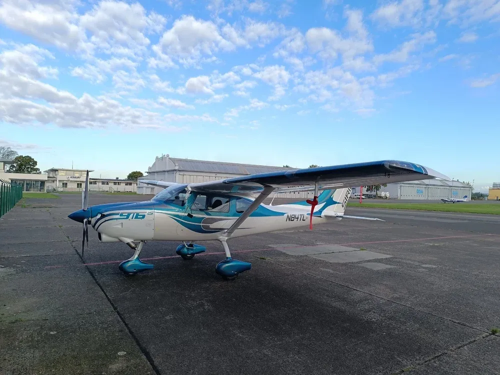 A white and teal Sirius 916 LS aircraft, registration N84TL, parked on an asphalt tarmac under a partly cloudy sky.