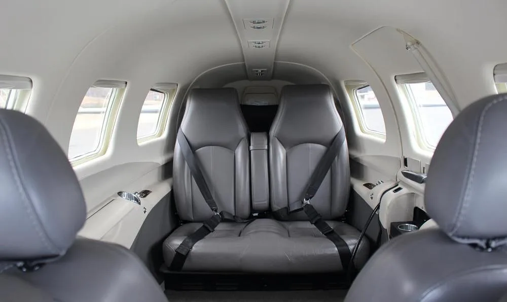 The aircraft's interior cabin with two rows of grey leather seats, viewed from the front.