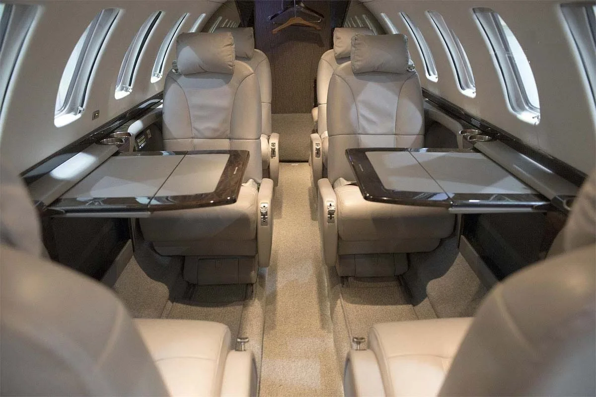 The luxurious interior cabin of a private jet with light-colored leather seats and fold-out tables.