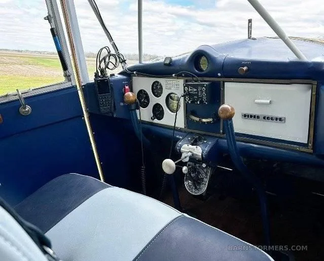 The blue and white interior of a vintage Piper aircraft cockpit, showing the seat, instrument panel, and controls.