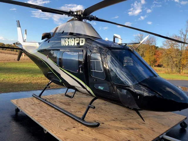 A black and silver Bell 429 helicopter with registration N319PD parked on a wooden pallet outdoors.