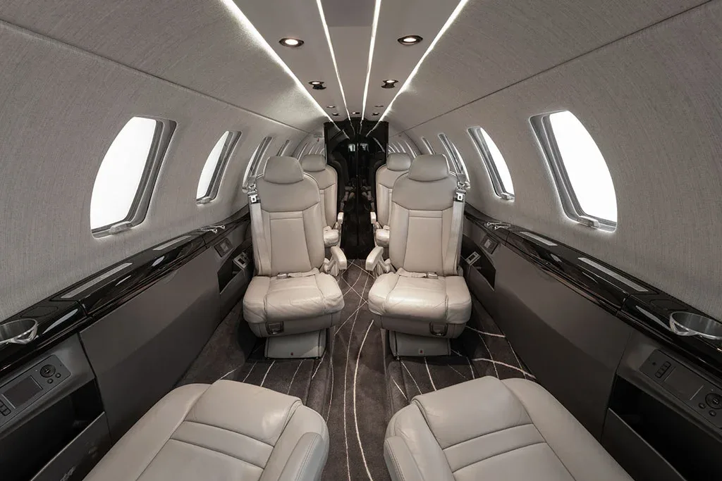 A view of the private jet's cabin interior, featuring light gray seats and a dark patterned aisle carpet, looking towards the rear.