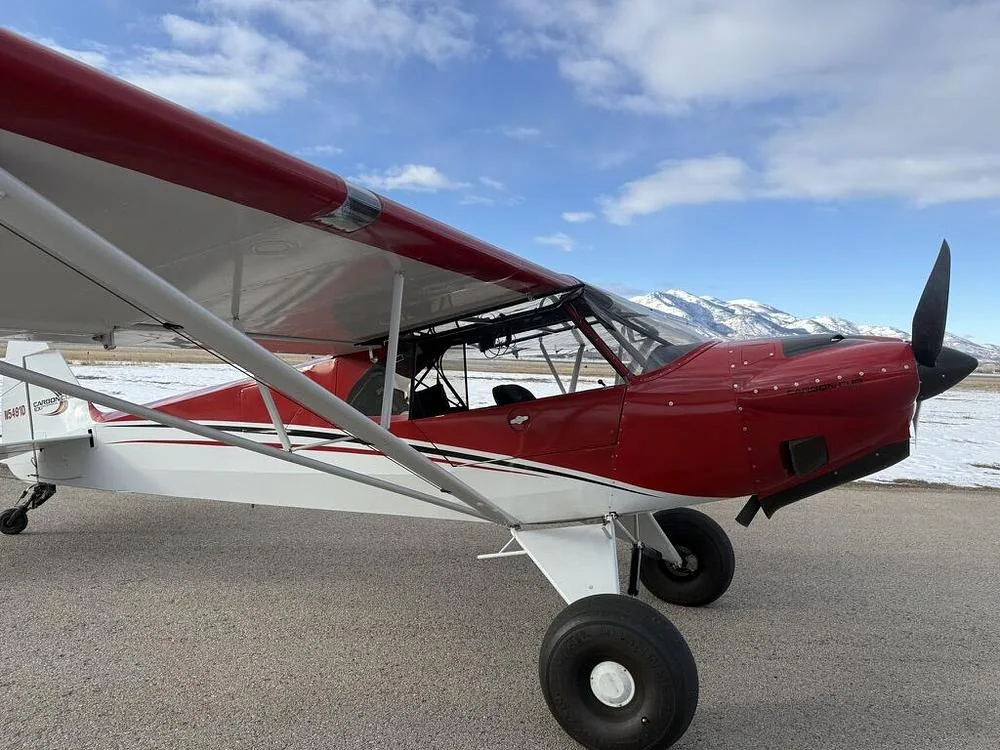 A close-up side view of a red and white bush plane with N5491D on the tail, parked on an asphalt runway.