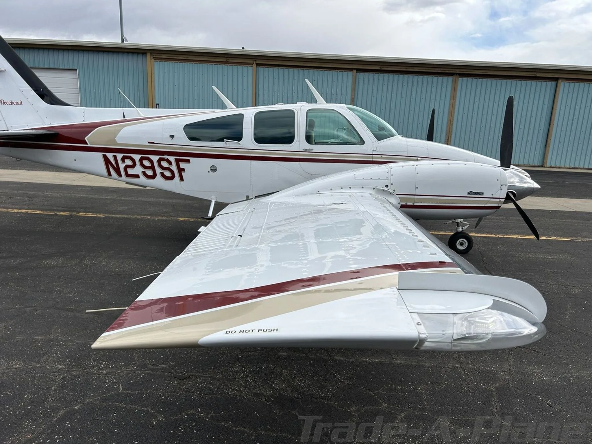 A side view of the white and maroon Beechcraft Baron N29SF, showing the right wing and fuselage, parked on an asphalt ramp.