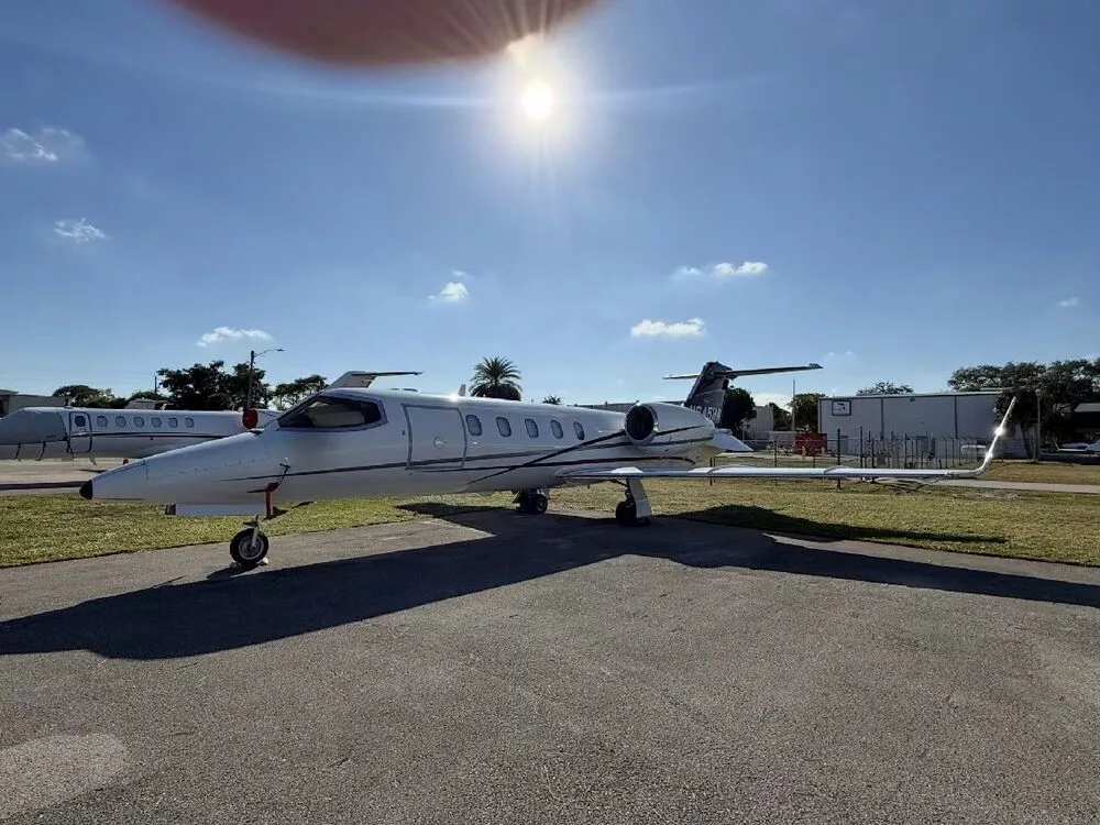 A white Learjet 35A aircraft with a dark tail parked on an asphalt ramp under a sunny sky.