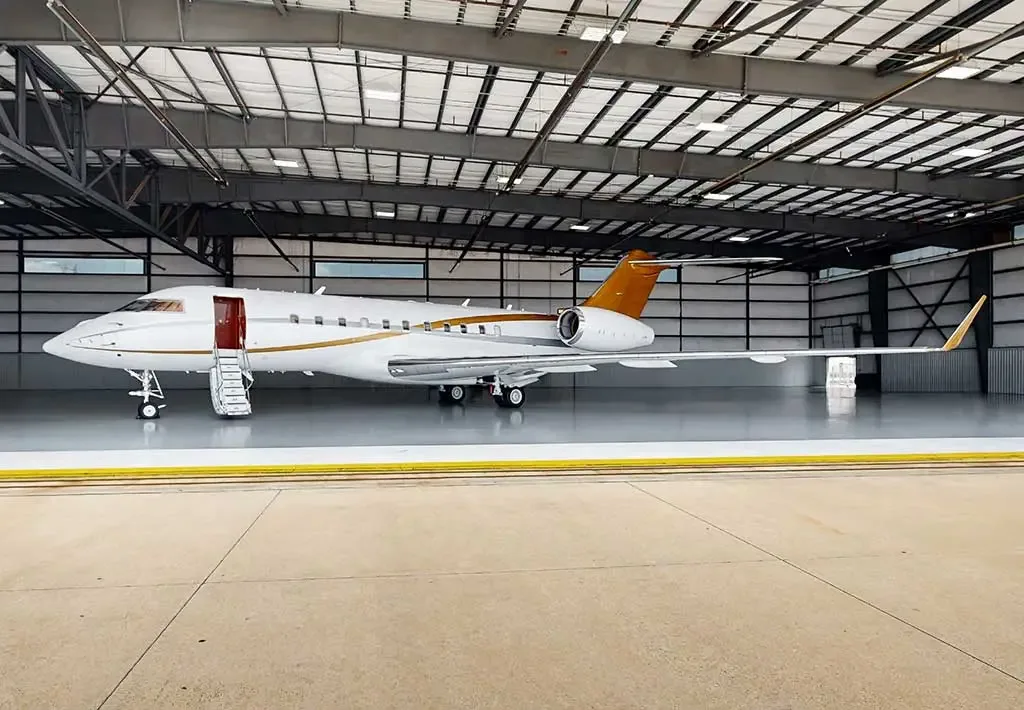 A white business jet with gold accents and an open door with stairs is parked inside a hangar.