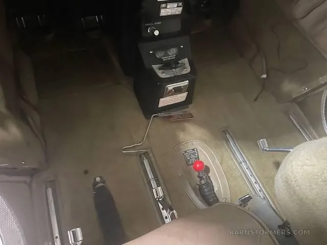 The tan carpeted floor of an aircraft cabin, showing the center console, rudder pedals, and control levers.