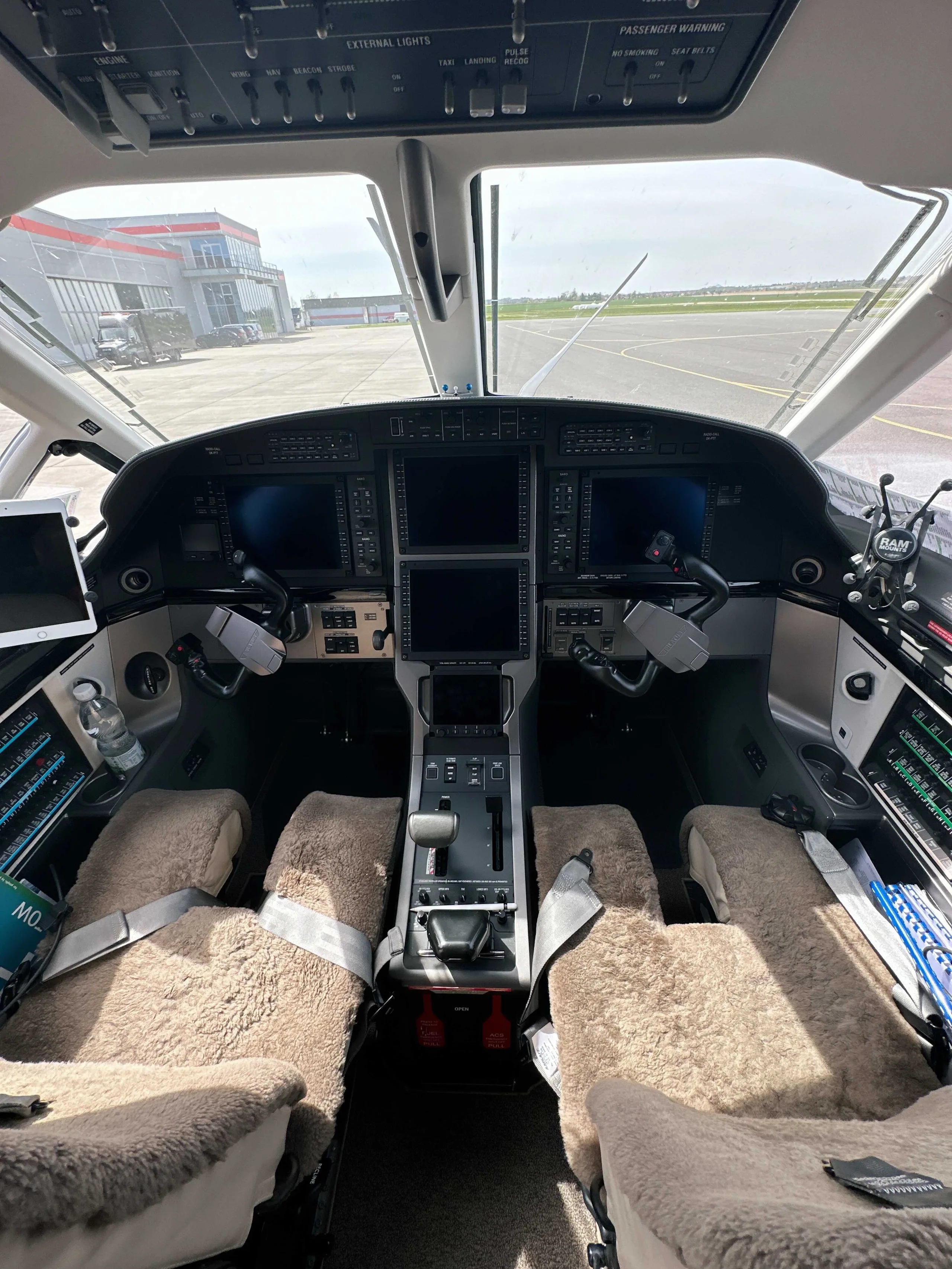 The cockpit of an aircraft featuring multiple digital displays, control yokes, and two pilot seats with sheepskin covers.