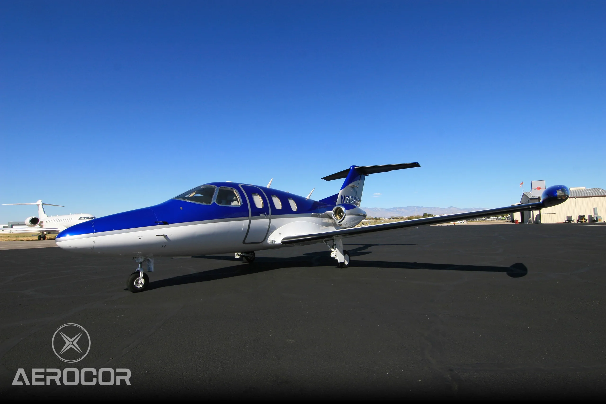 A blue and white Eclipse 500/550 jet, N712WG, parked on an airport tarmac under a clear blue sky.