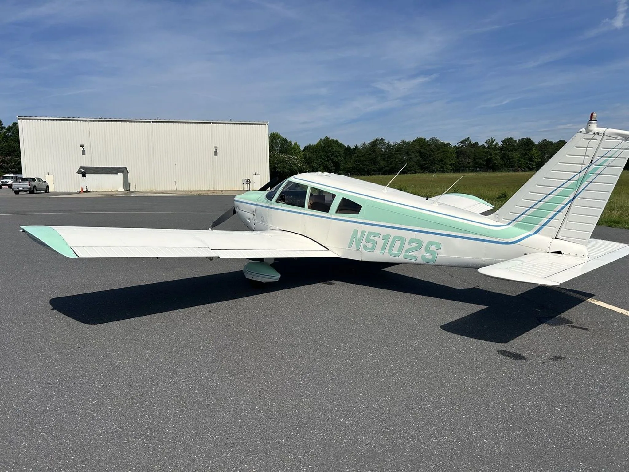 The Piper Cherokee 180 with a hangar in the background.