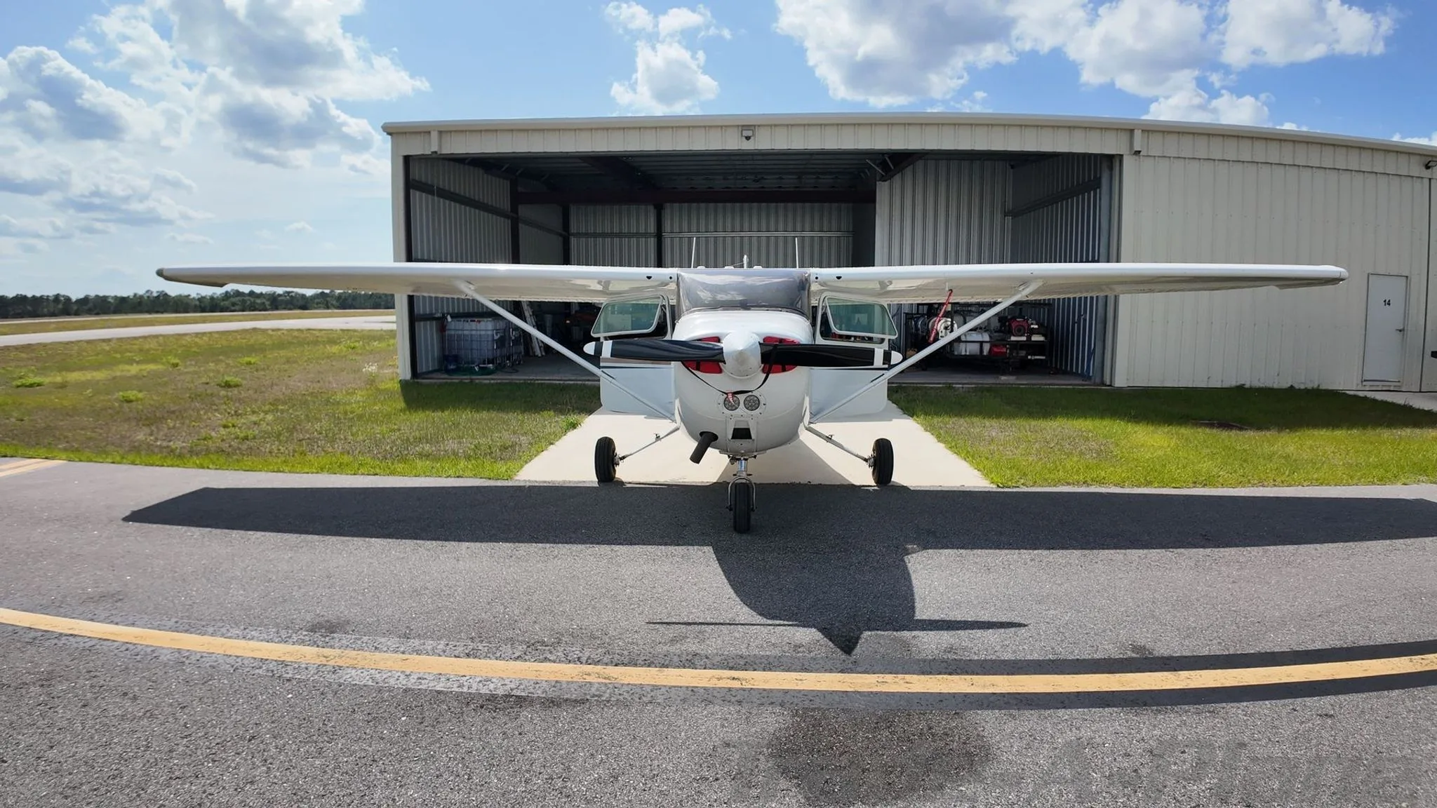 A head-on view of a white Cessna 172 Skyhawk with brown and blue stripes, tail number N737KE, parked in front of a hangar.