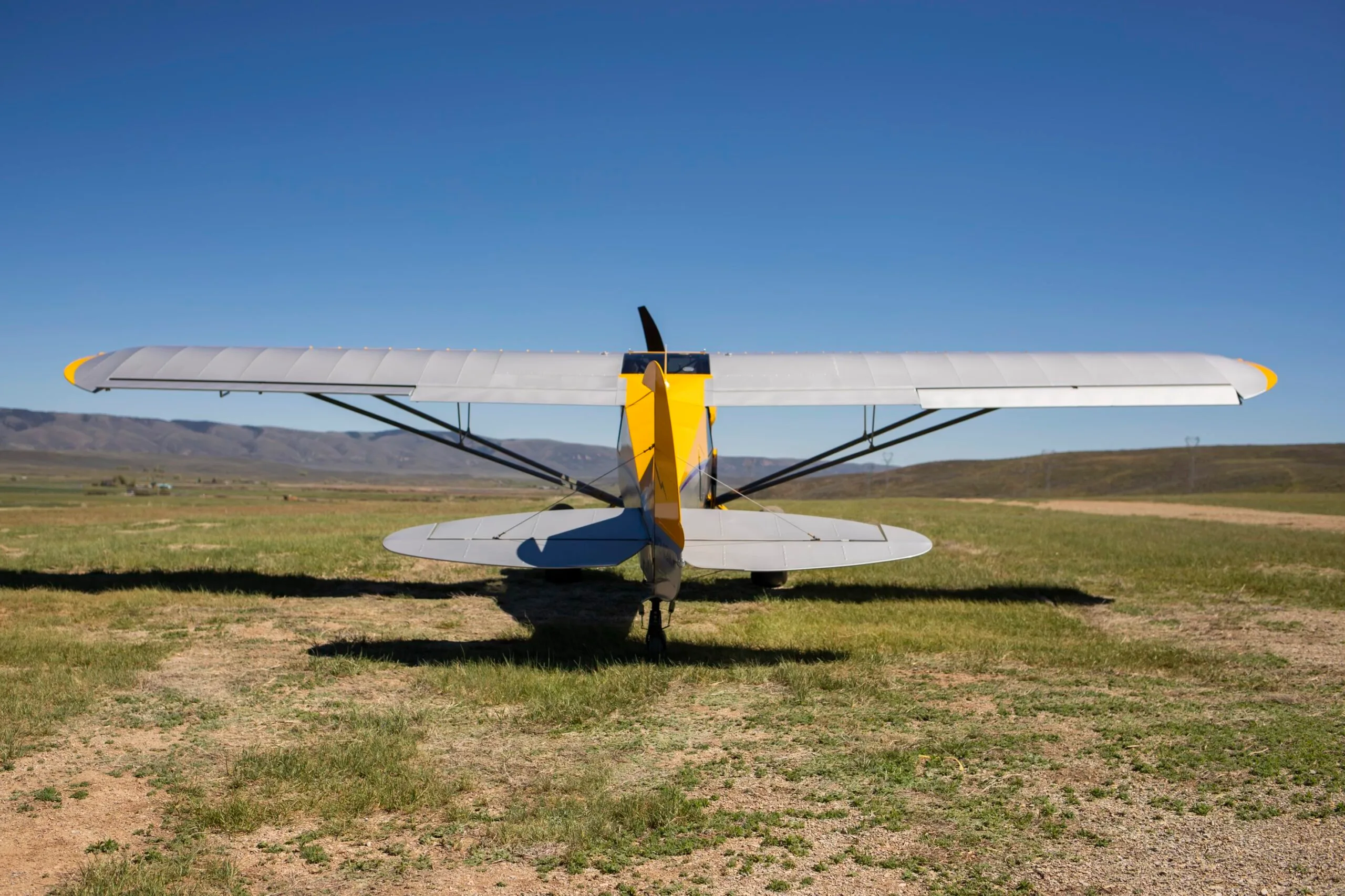 A rear view of a yellow and silver CubCrafters XCub aircraft parked on a grassy field.