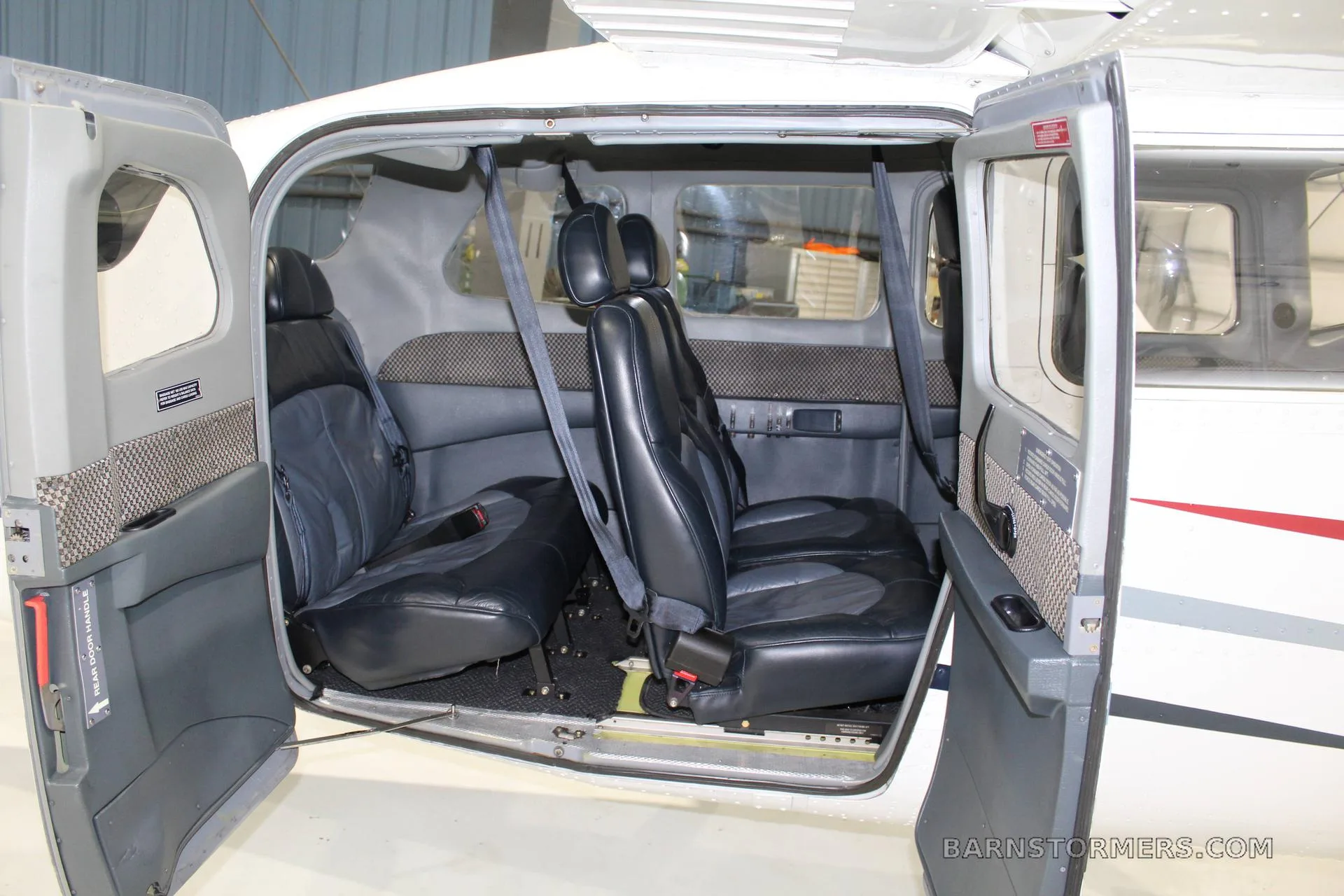 The interior cabin of a small aircraft showing two rows of black leather seats with the doors open.