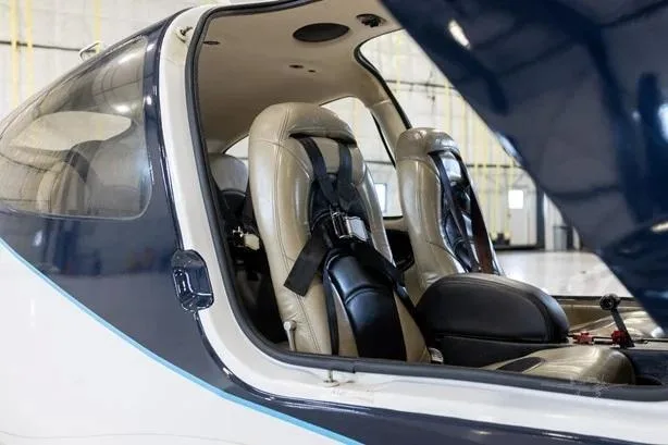 Close-up view of the tan leather interior seats with black harnesses inside a dark blue and white aircraft.