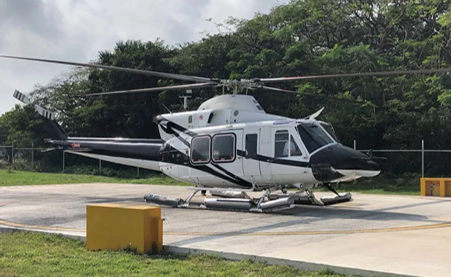 A Bell 412 helicopter parked on a helipad with trees in the background.