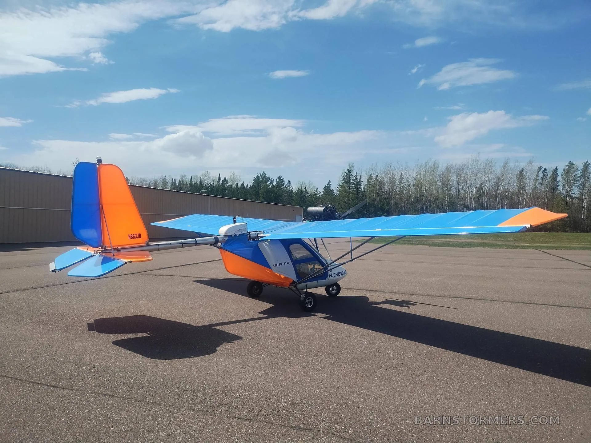 A blue and orange Flightstar II SC ultralight aircraft, tail number N663JD, viewed from the rear on an airfield.