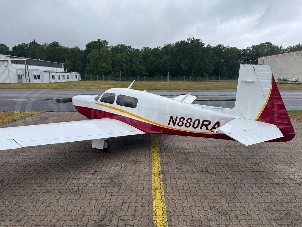 The rear-side view of a white and red single-engine aircraft, N880RA, parked on a paved tarmac.