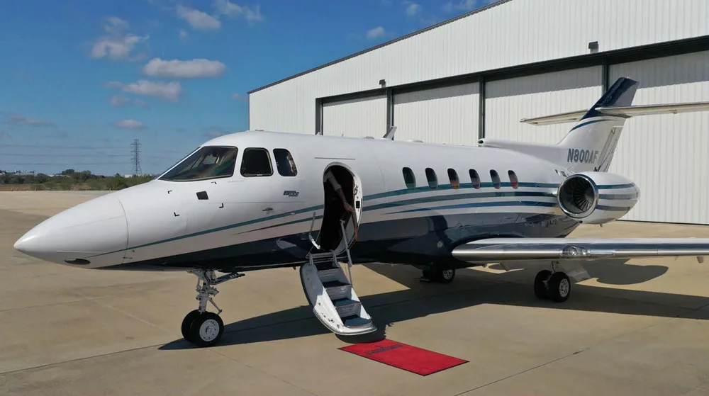 A white and blue Hawker 800XP business jet, registration N800AF, with its door open and stairs extended, parked in front of a hangar.