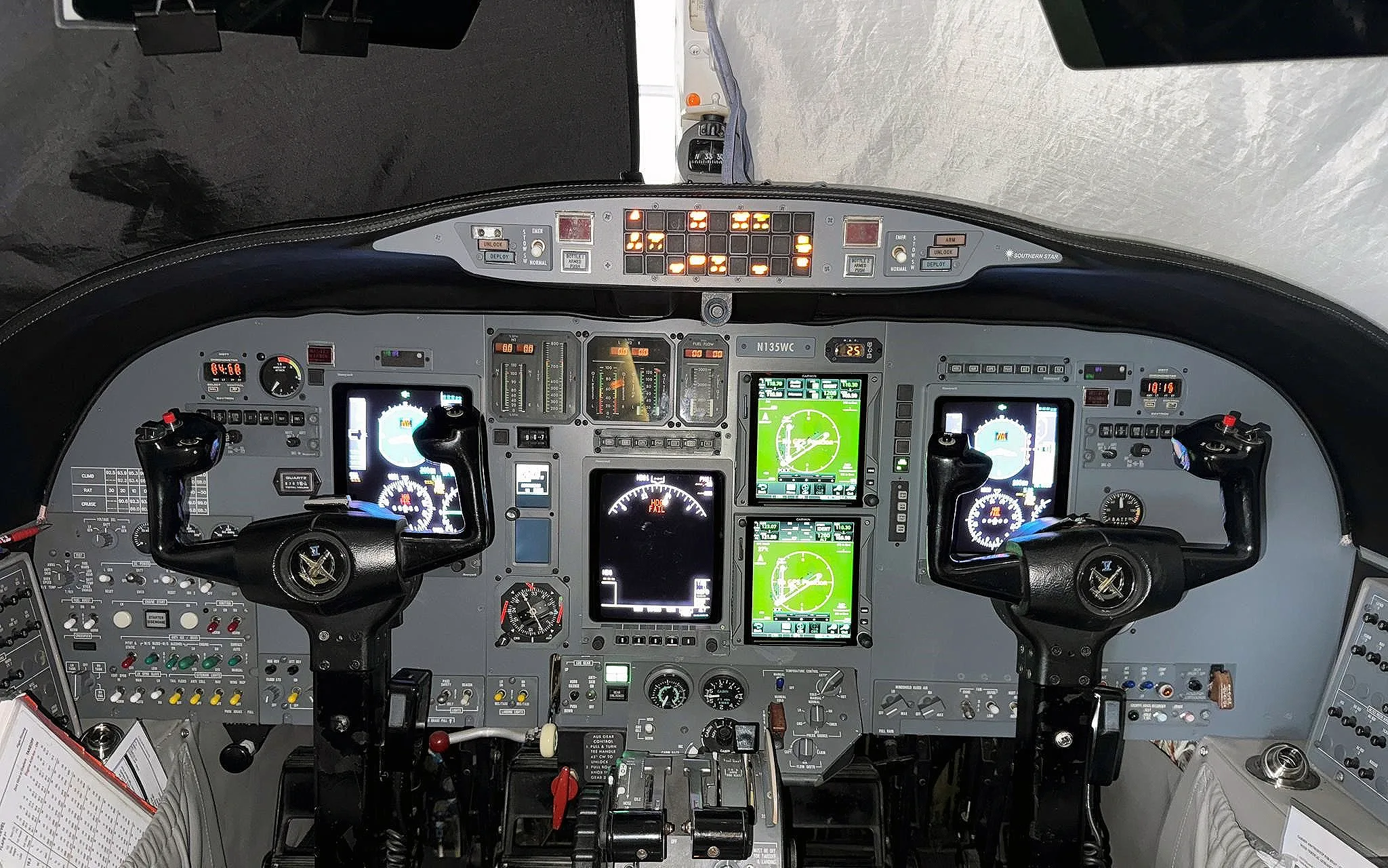 The cockpit of a private jet, featuring multiple display screens and control yokes.
