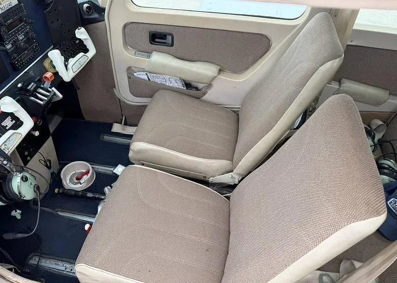 The front cabin interior of a Beechcraft Sundowner N37240, showing two tan fabric seats and part of the cockpit.