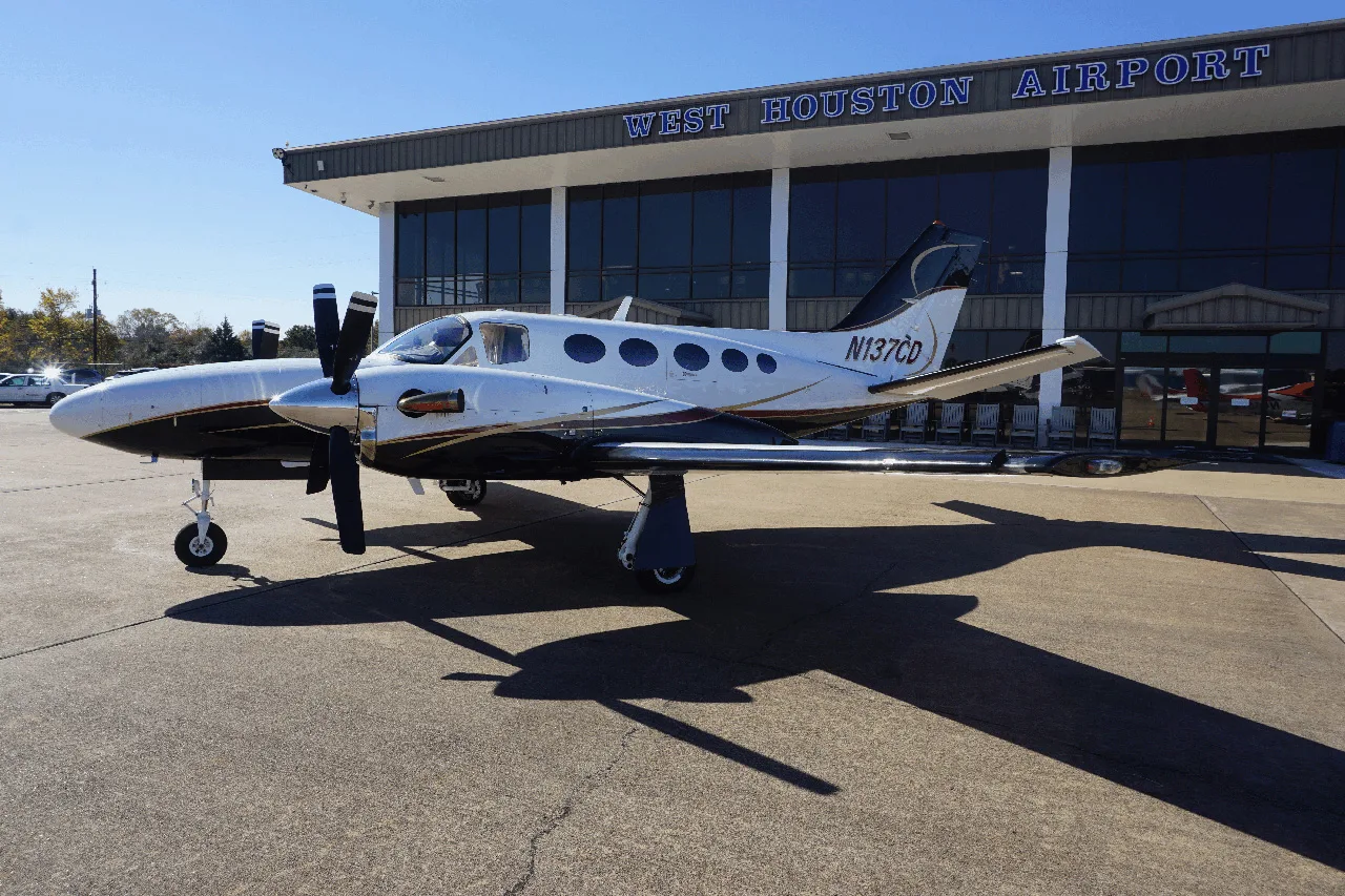 A white and black Cessna Conquest I (N137CD) parked on the tarmac in front of the West Houston Airport building.