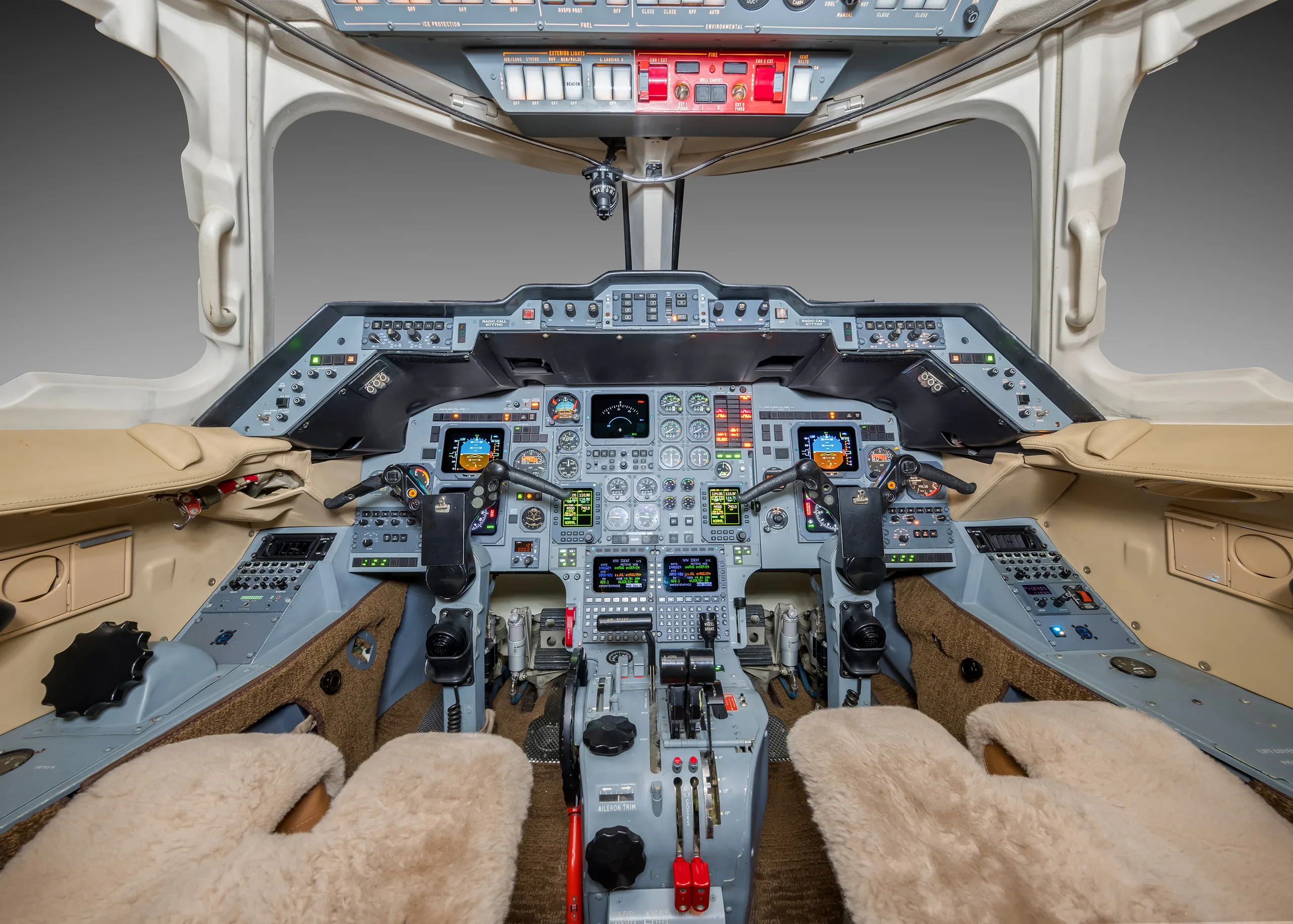 The cockpit of a business jet with multiple screens, instruments, and tan sheepskin seat covers.