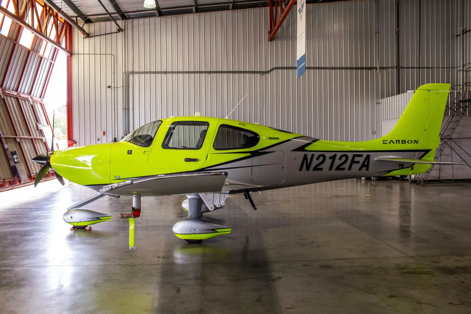 Side view of a bright yellow and silver Cirrus SR20 aircraft with registration N212FA in a hangar.