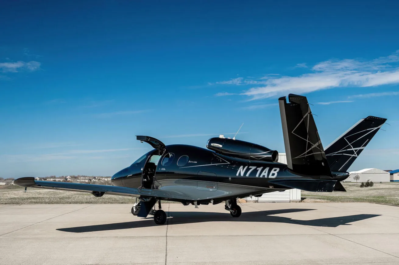 A black Cirrus Vision Jet (N71AB) with a grey underside and geometric tail design, parked on an airport tarmac with its main door open.