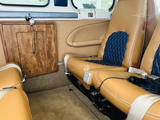 The aircraft's interior cabin with tan leather seats featuring blue diamond-stitched inserts and a wooden cabinet.