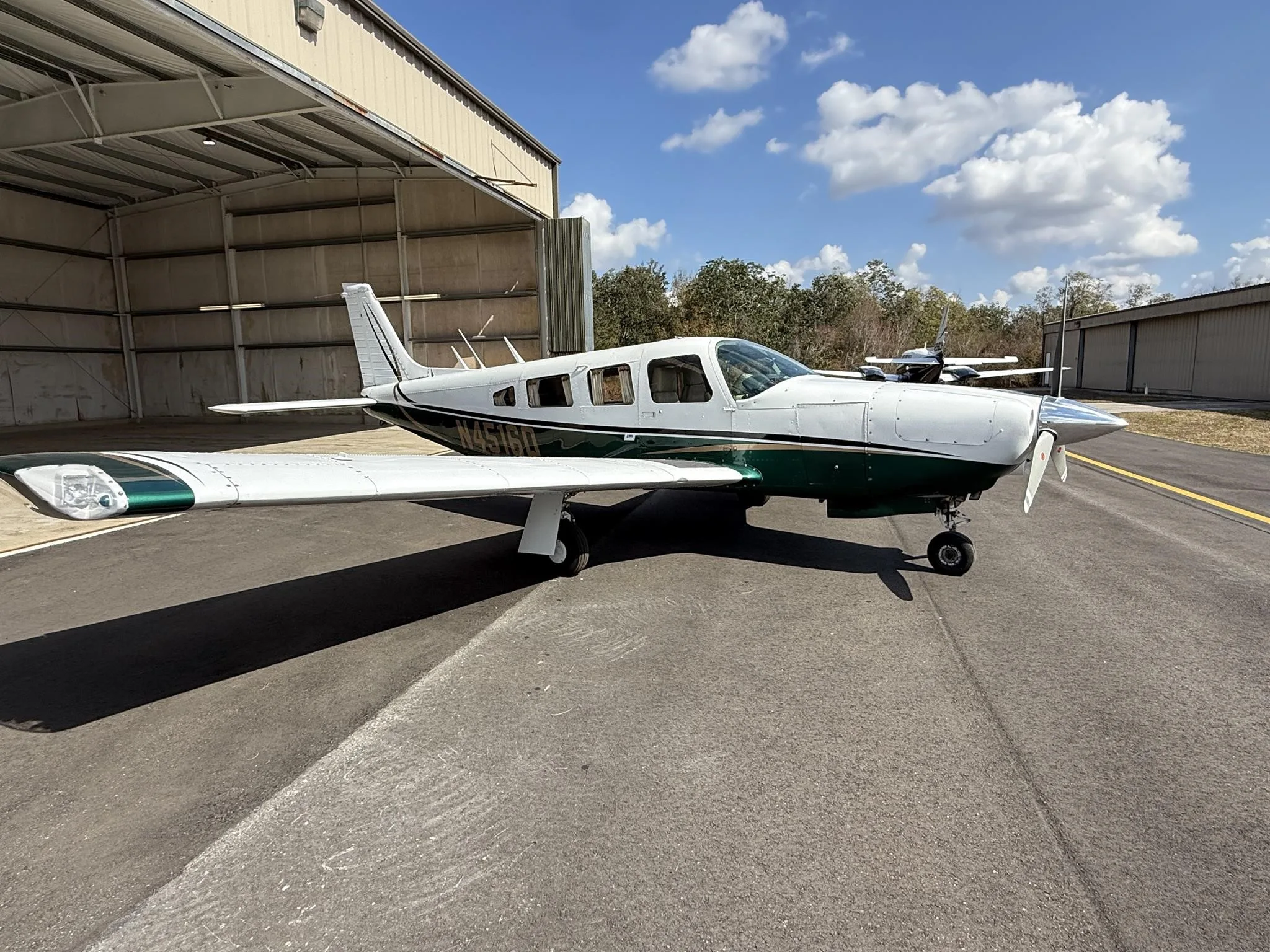 A white and green Piper PA-32R-300 Cherokee Lance II (N4516Q) parked on an asphalt ramp with another aircraft in the background.