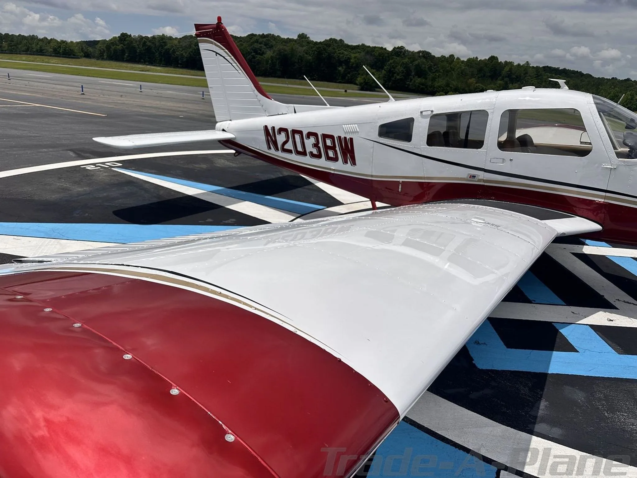 A close-up view of the tail and wing of the white and red aircraft N203BW on an airport tarmac.