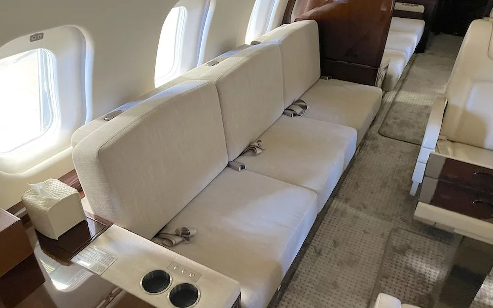 A close-up view of a cream-colored three-seat sofa in a private jet cabin next to a window.