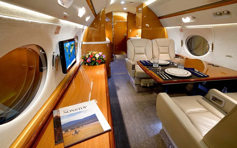 The aircraft's dining area with a set table, a bouquet of flowers, and a wall-mounted TV displaying a world map.