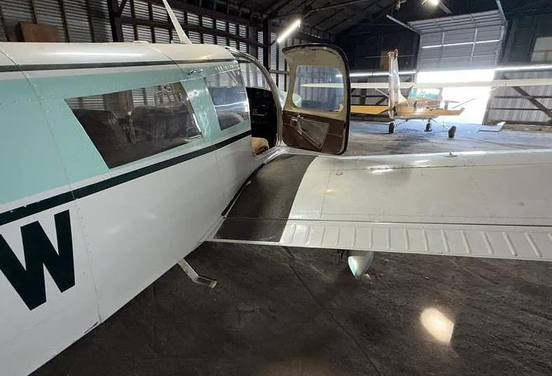 Side view of a Piper Cherokee Six with its door open, parked in a hangar.