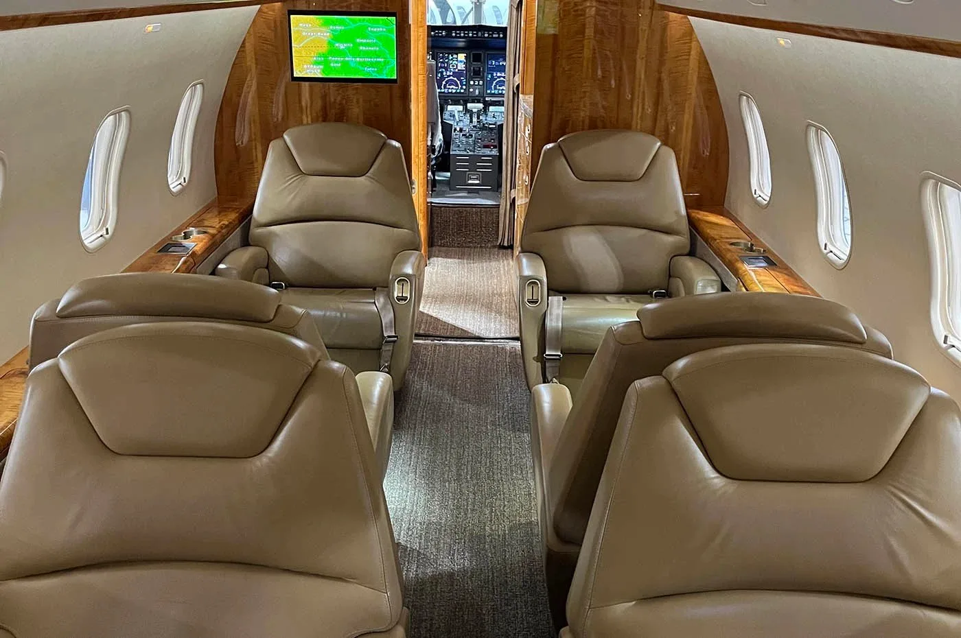 The luxurious interior cabin of a business jet with tan leather seats and wood paneling, looking towards the cockpit.