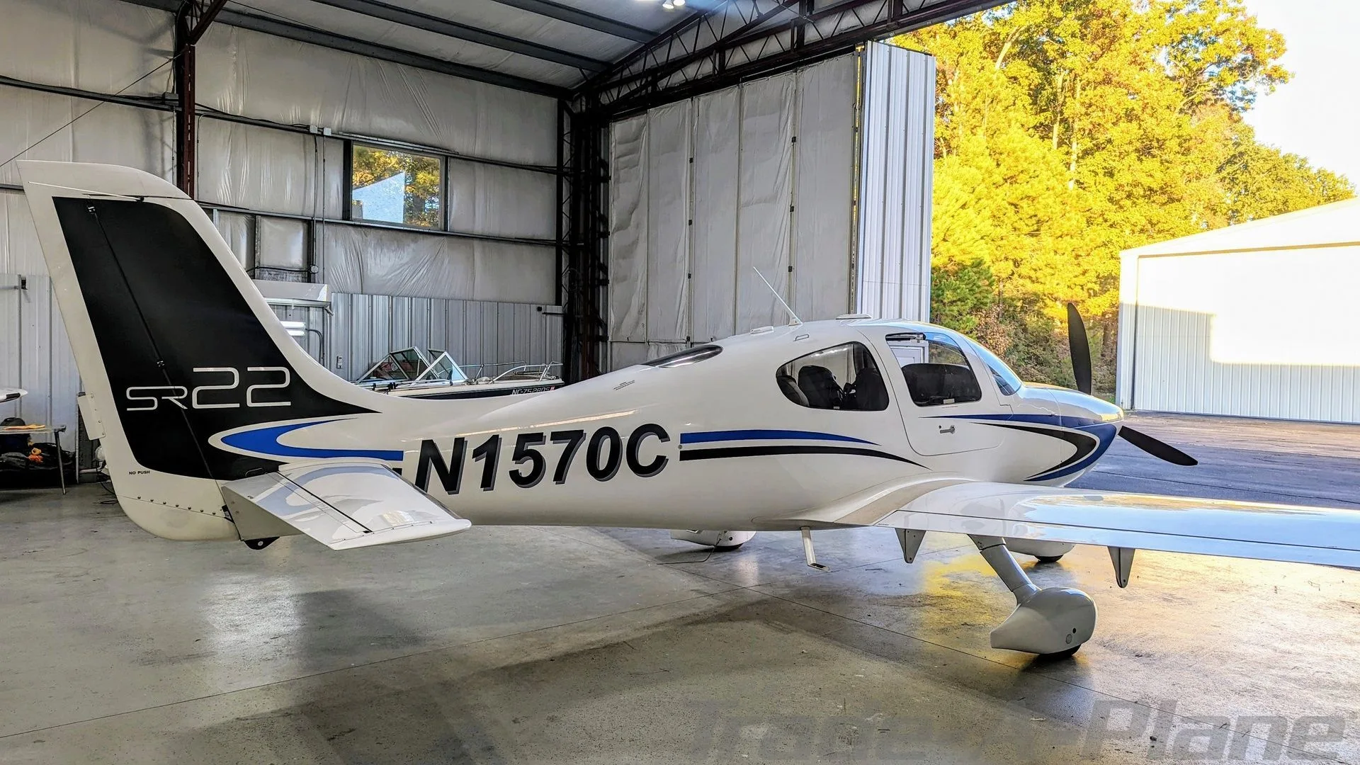 Rear view of a white Cirrus SR22 aircraft with blue and black stripes, registration N1570C, partially outside a hangar.