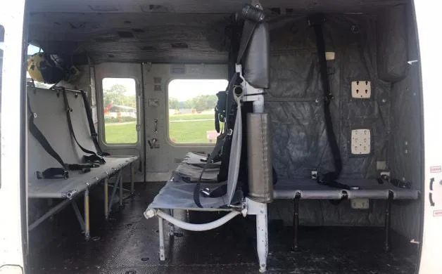 The interior cabin of a helicopter with grey utility seating and visible windows.